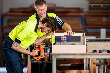 Supervisor with young male on carpenters workbench